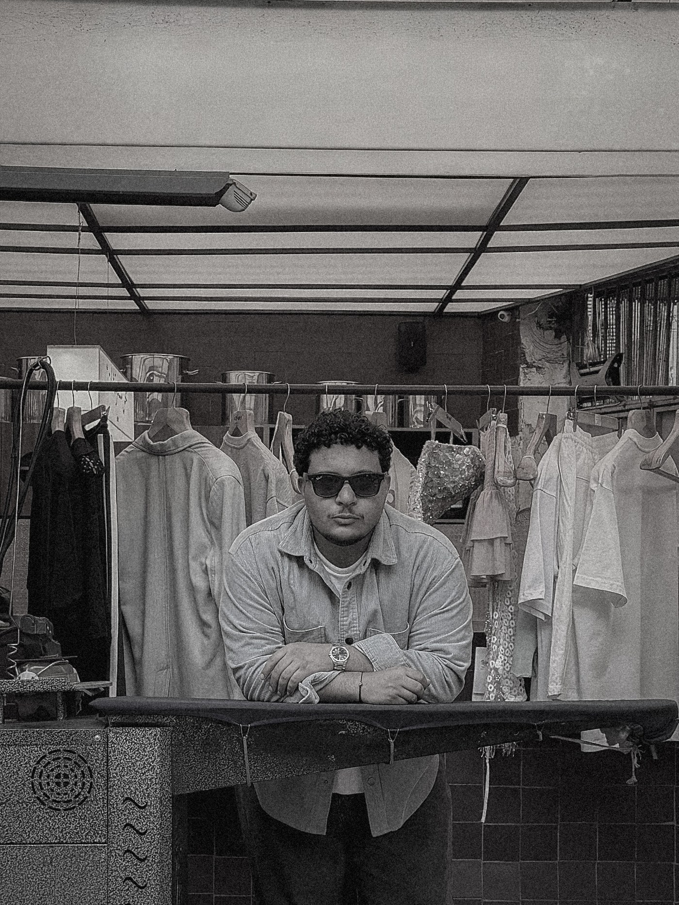 Zeyad Erekat in sunglasses leaning on an ironing board in a laundry shop, black and white