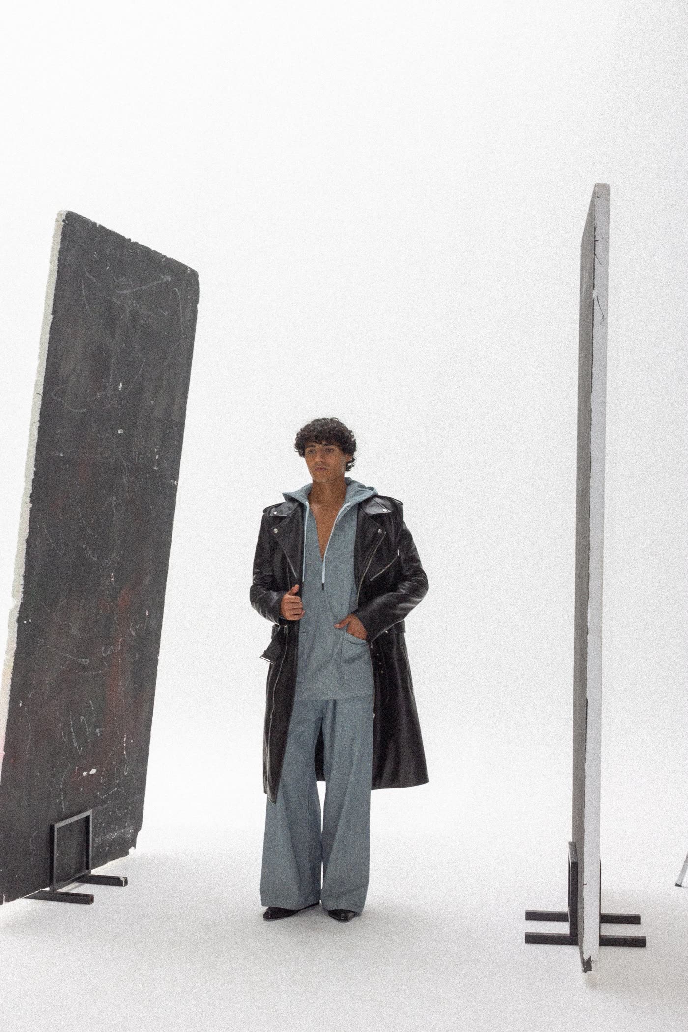 Model in a long black leather coat between two standing panels