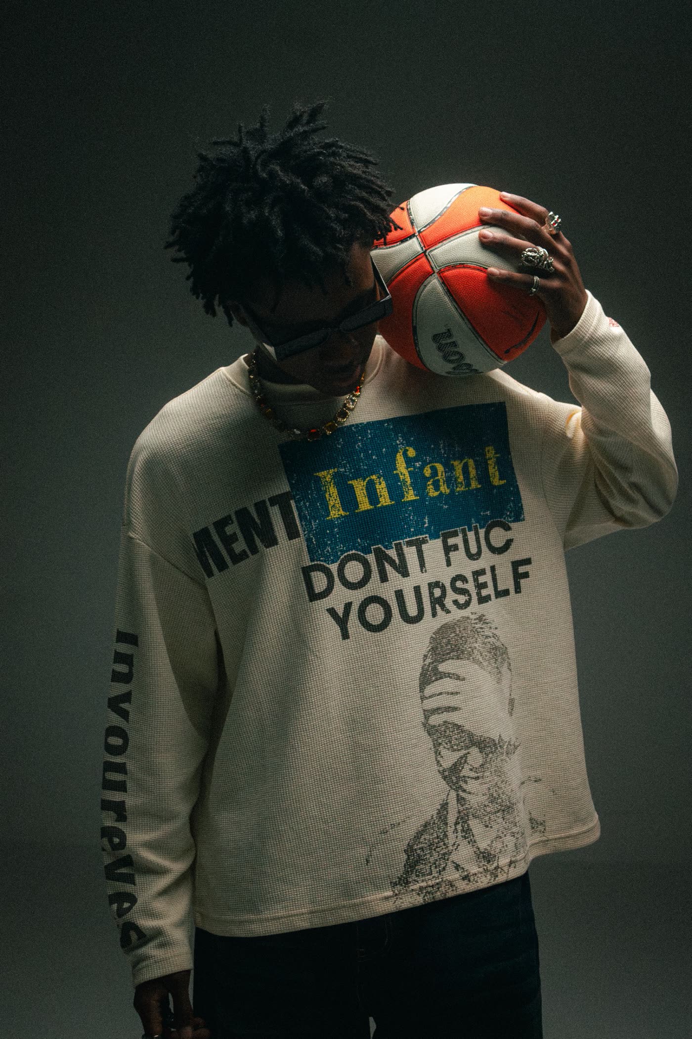 Man in a graphic long-sleeve top holding a basketball to his head