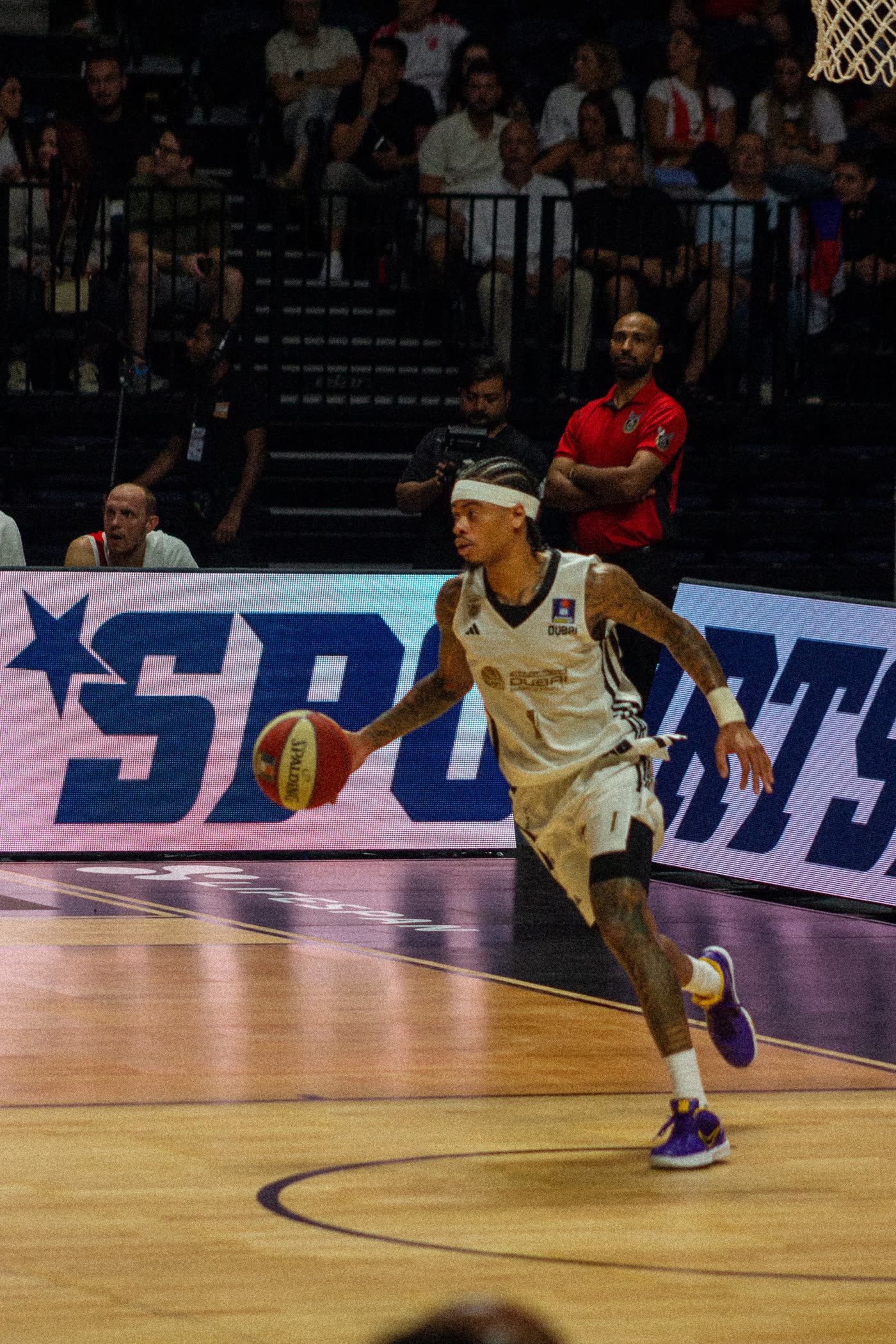 Dubai Basketball guard in a white adidas kit dribbling past the courtside boards