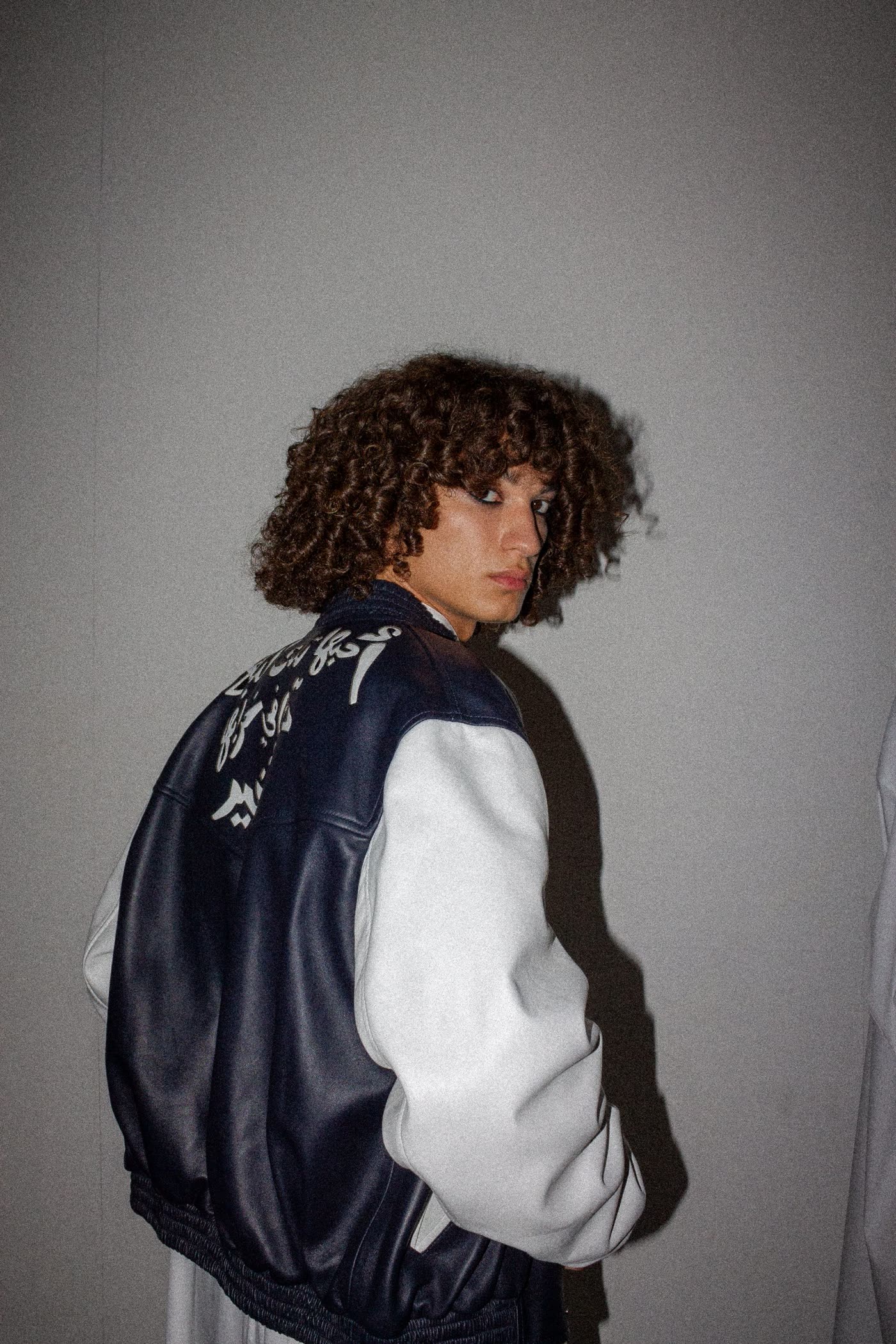 Model in a navy and white varsity jacket with Arabic script