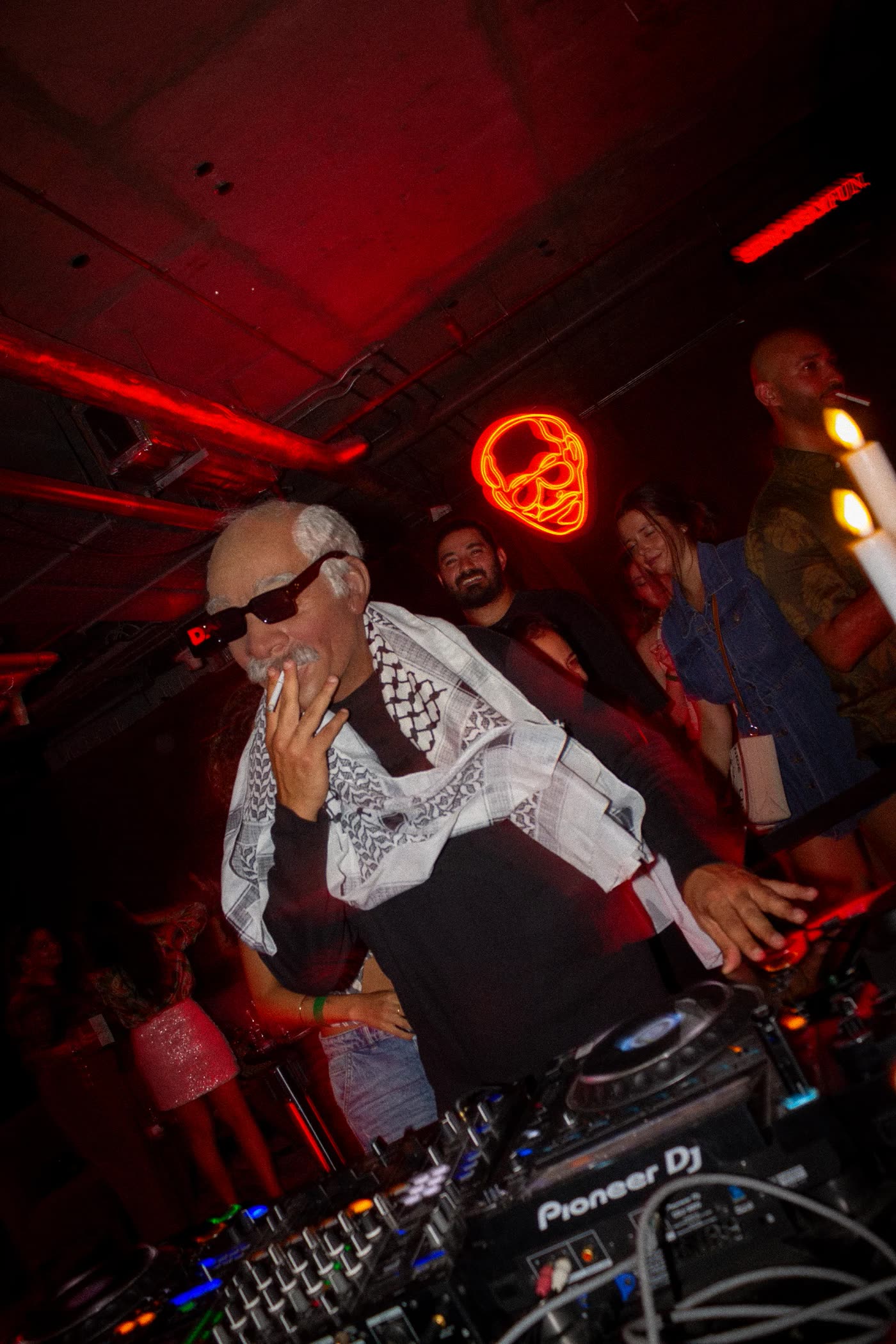 DJ in a keffiyeh under red light and a neon skull