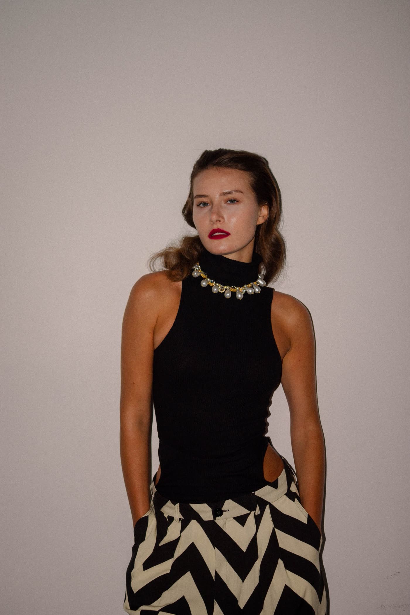 Model in a black turtleneck, pearl collar and zigzag trousers