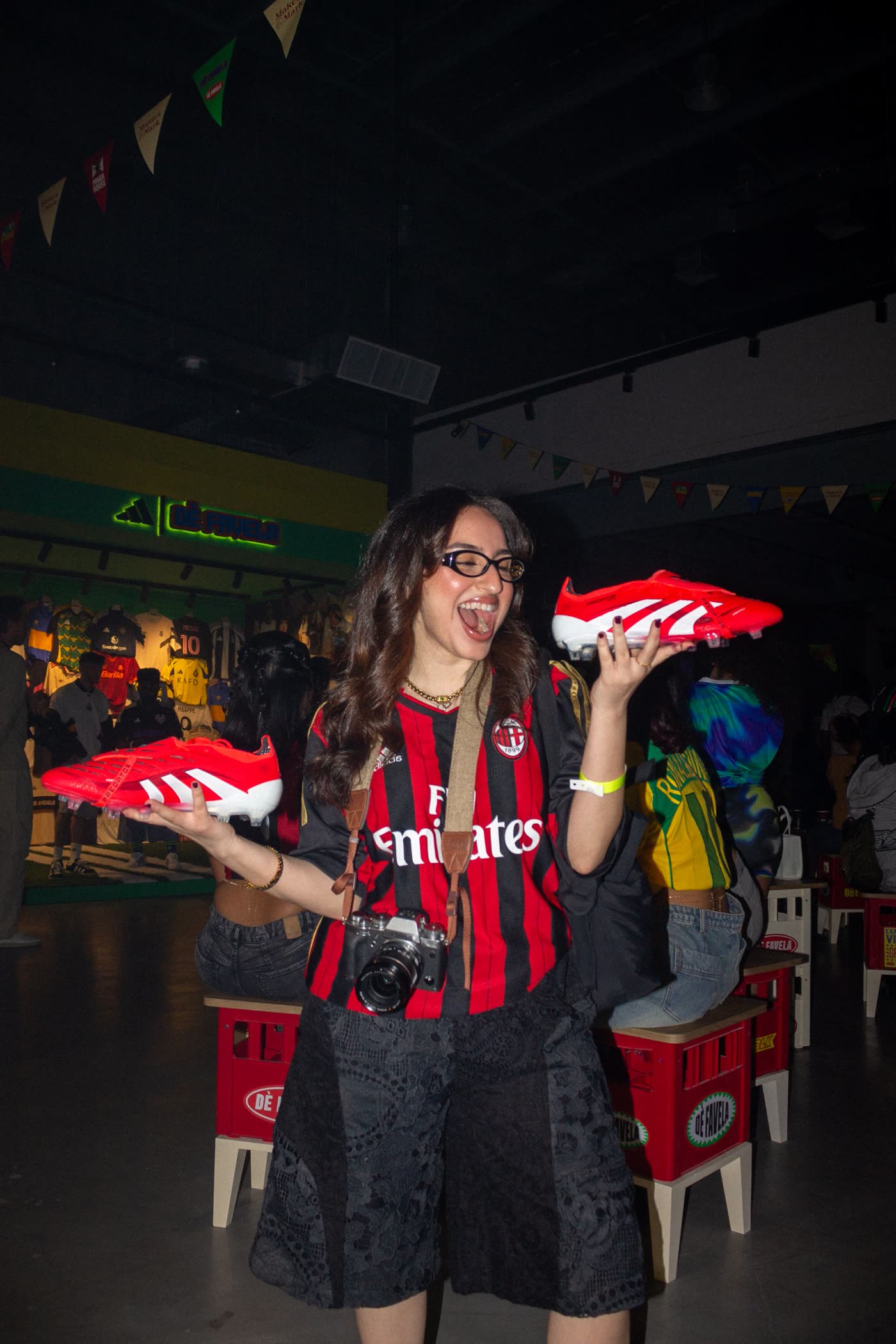 Guest in an AC Milan shirt with a camera, laughing and holding up two red Predator boots