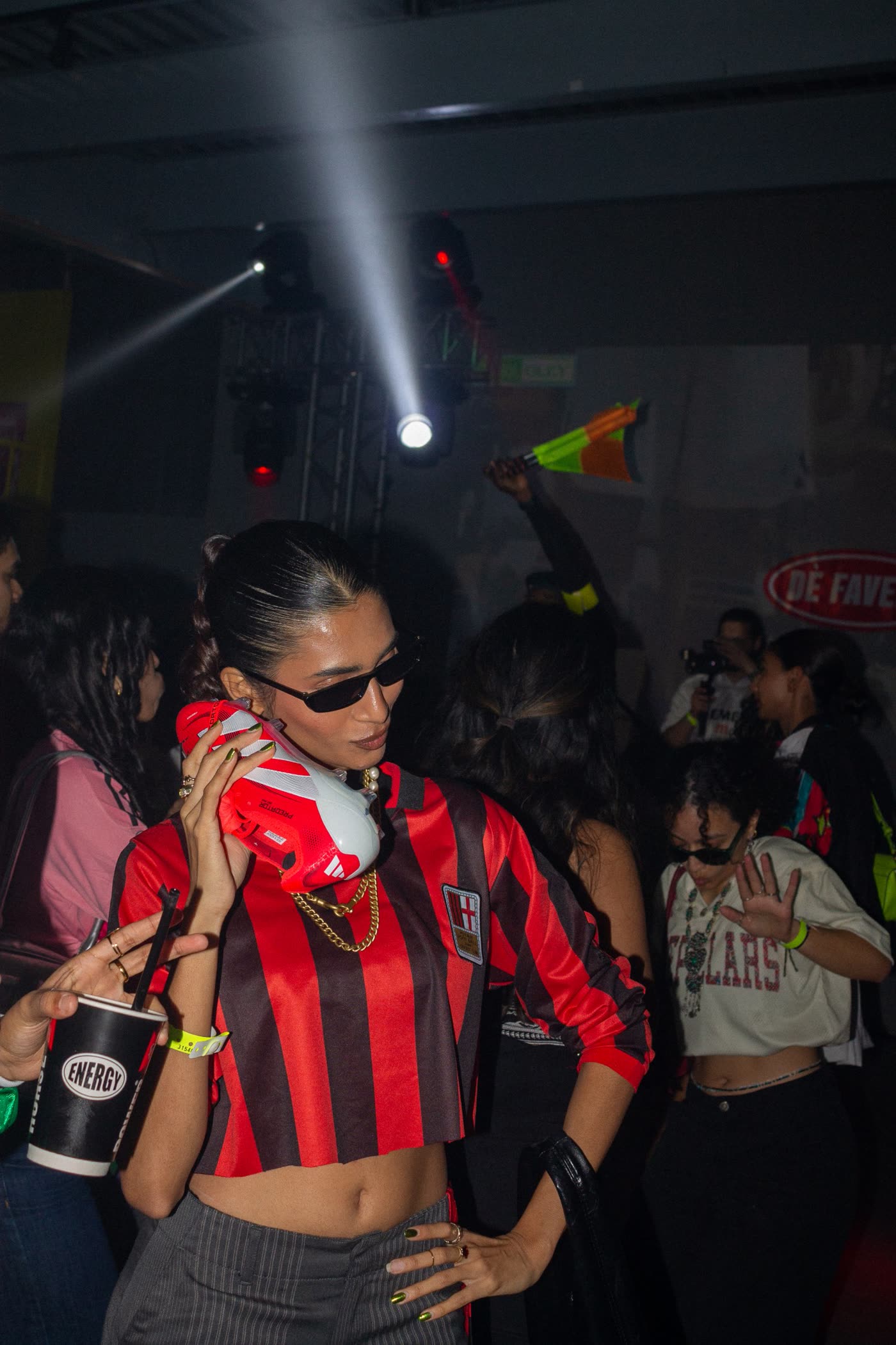 Guest in a striped football crop top holding a Predator boot to her ear like a phone