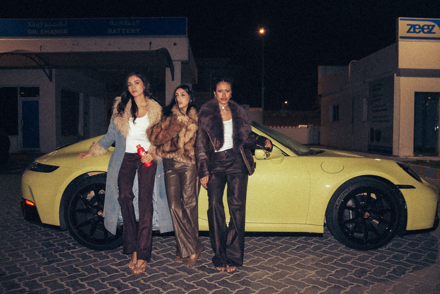 Three women standing by a yellow Porsche at night