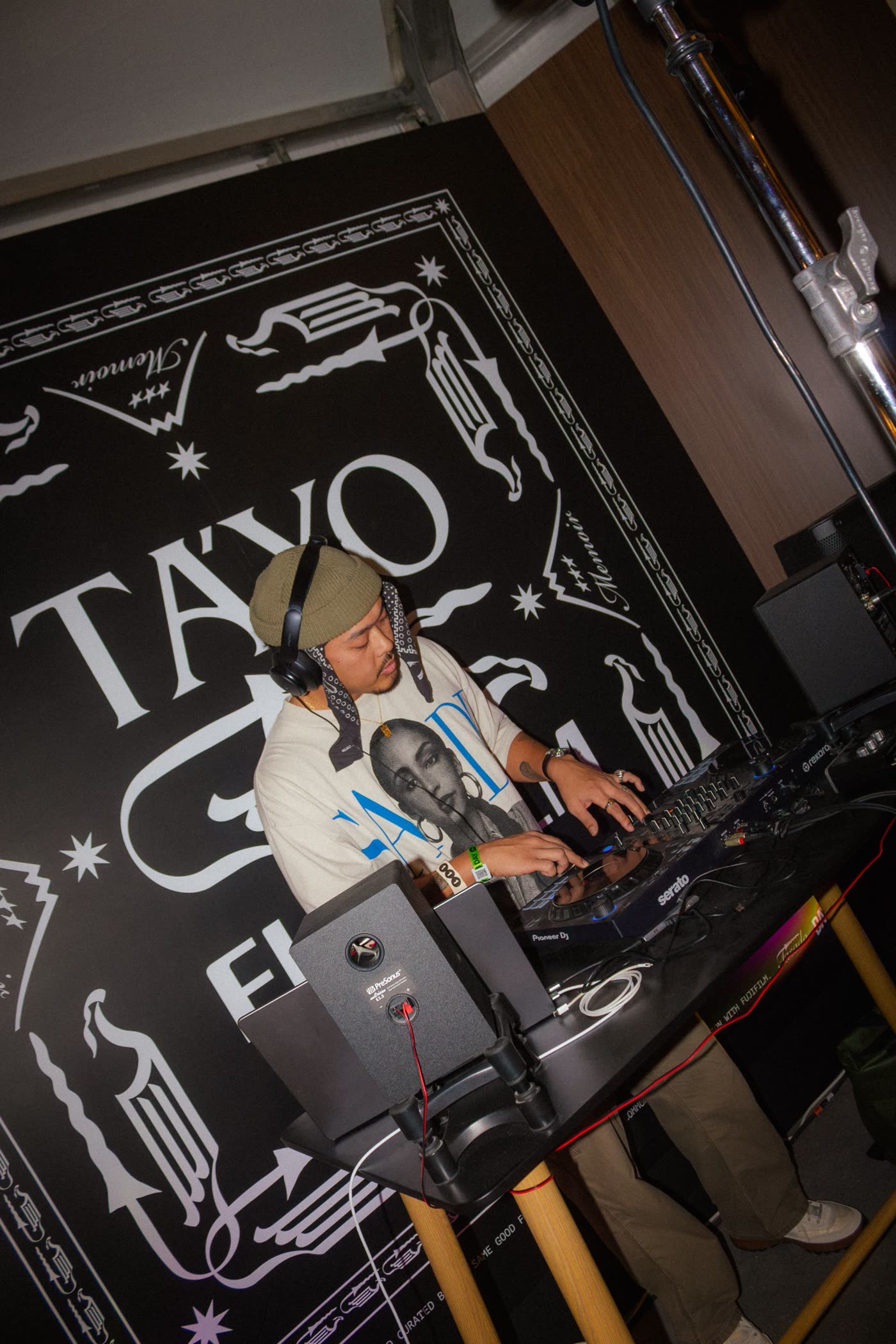 DJ in a green beanie and headphones playing in front of a black and white illustrated backdrop