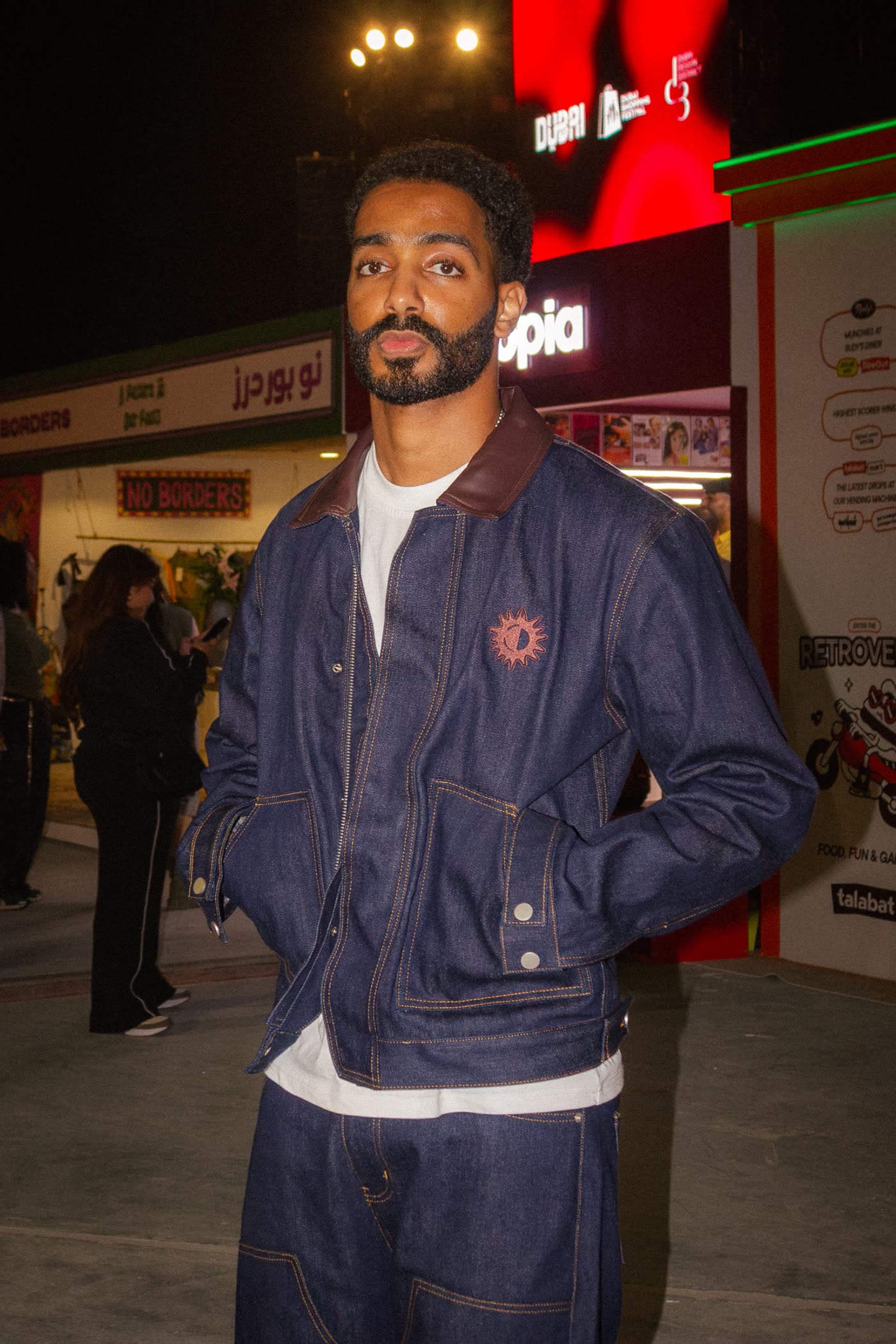 Man in a raw denim jacket with a leather collar standing among the festival stalls