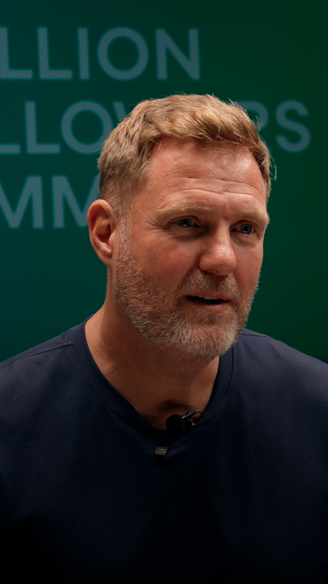 Close-up of Simon Squibb mid-sentence against a green backdrop