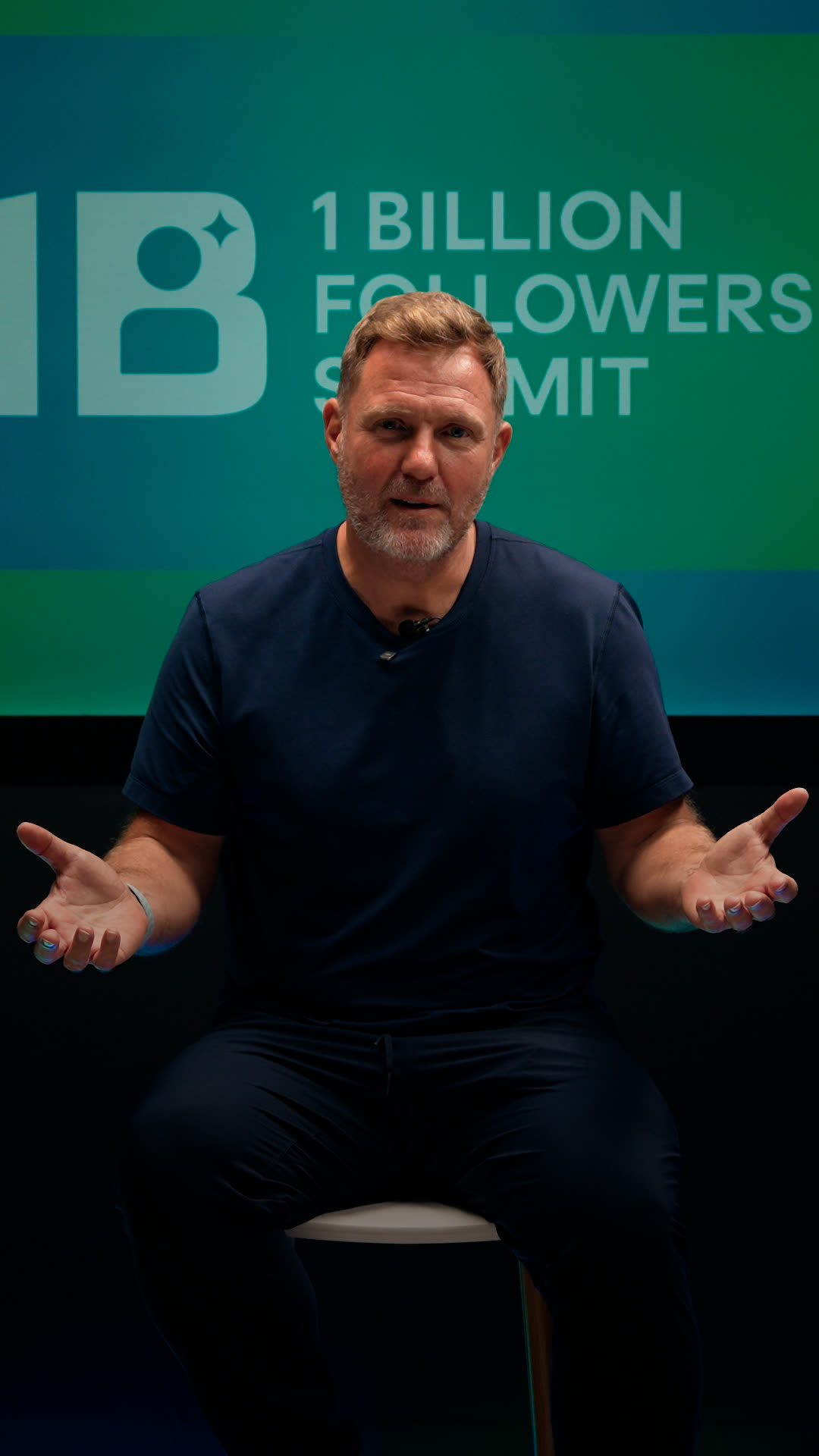 Simon Squibb seated on a stool in front of the 1 Billion Followers Summit screen
