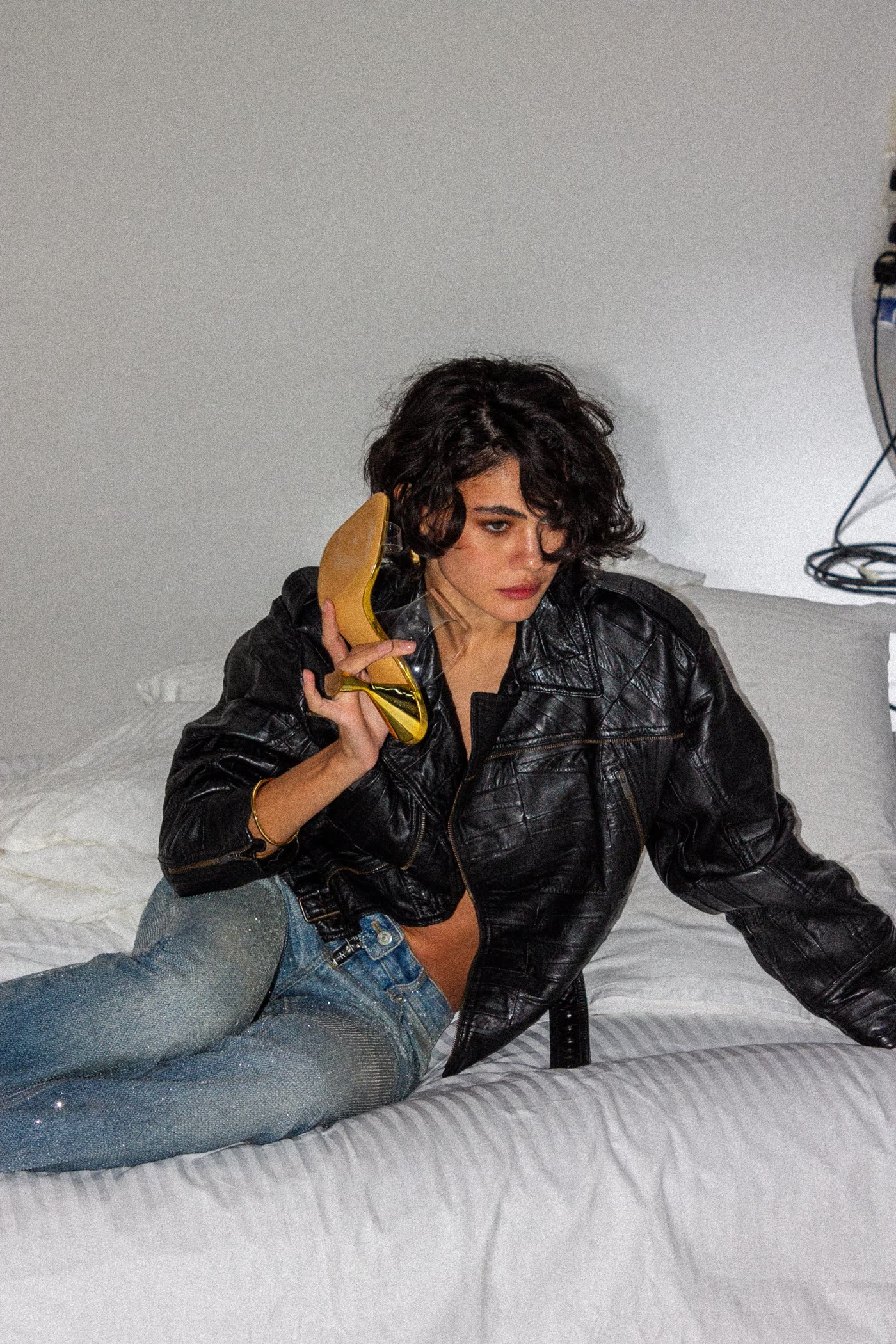 Model in a leather jacket holding a gold heel to her ear