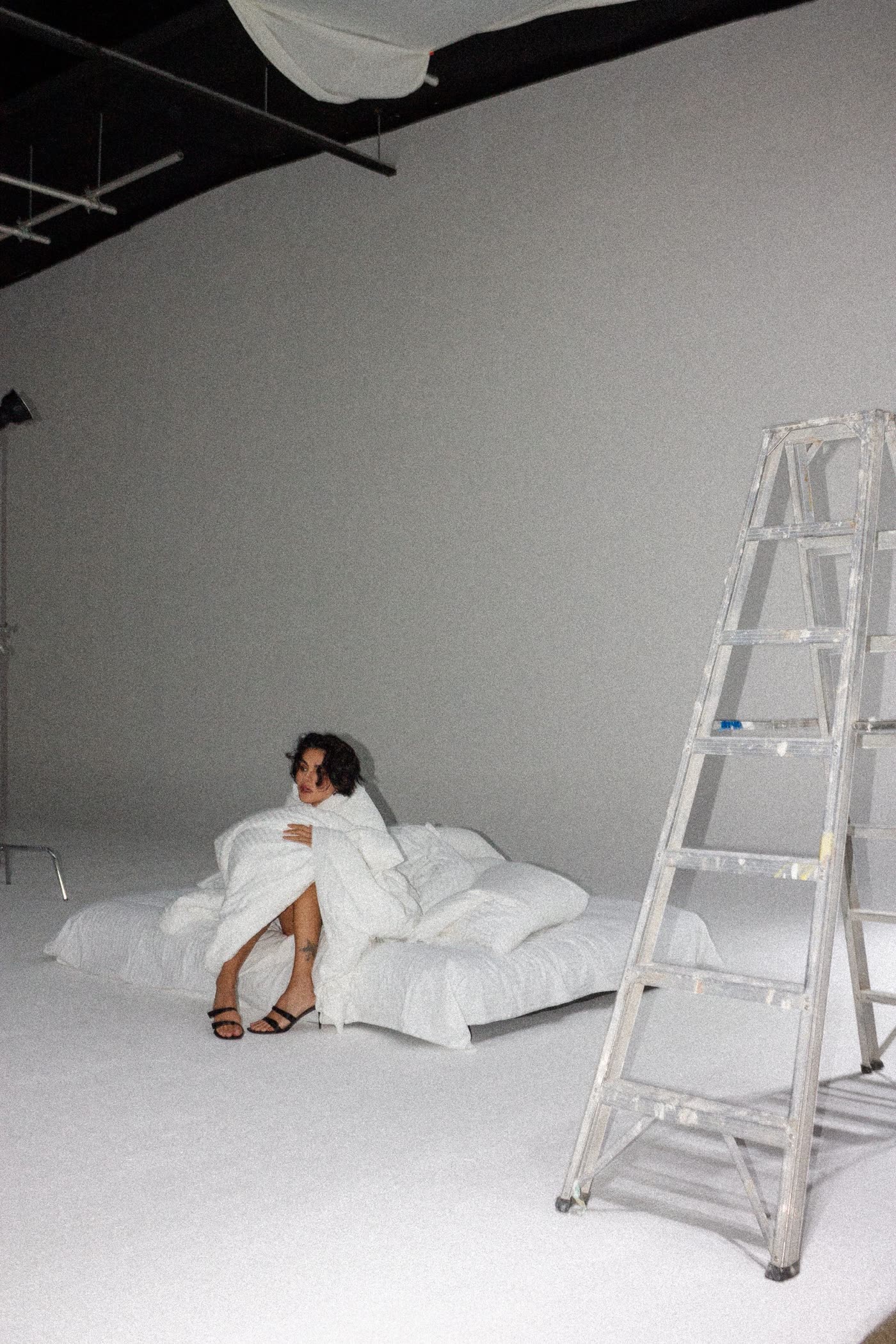 Model on a white bed beside a studio ladder