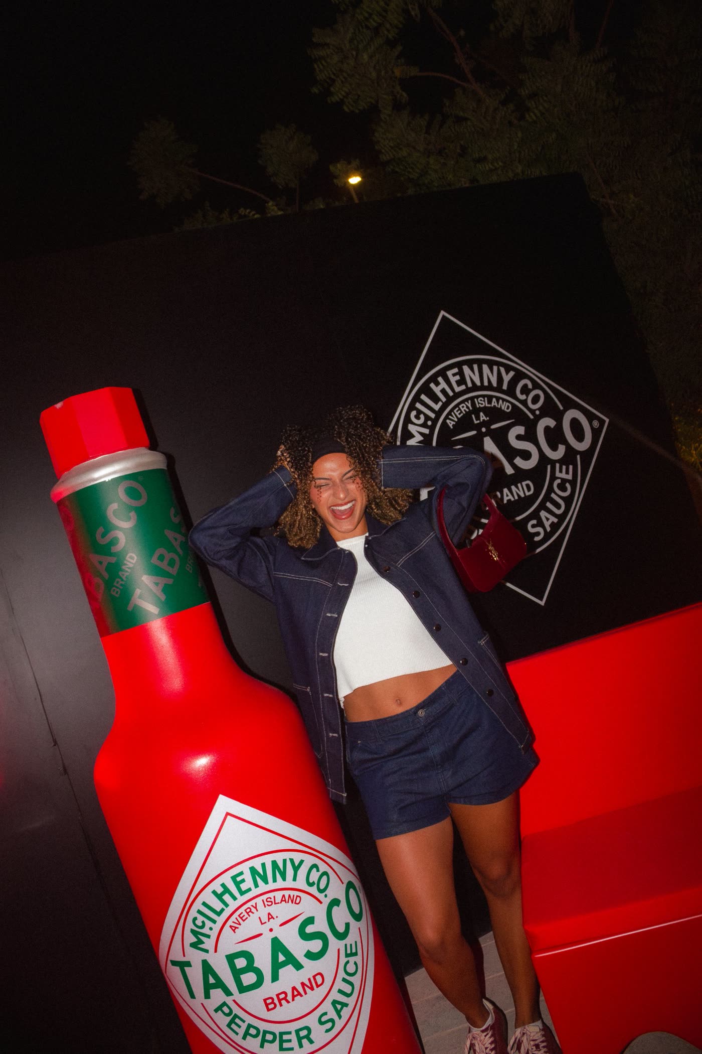 Guest in a denim set laughing beside a giant Tabasco bottle and the Tabasco logo