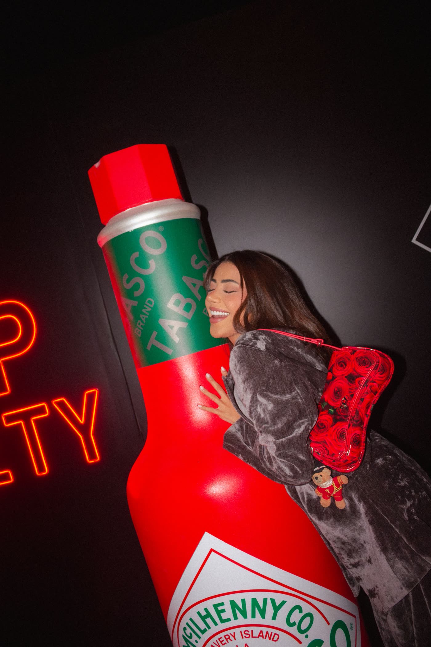 Guest in crushed velvet hugging a giant Tabasco bottle next to a neon sign